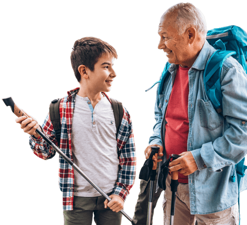 A man and a young boy smile while looking at each other. They are both holding hiking sticks